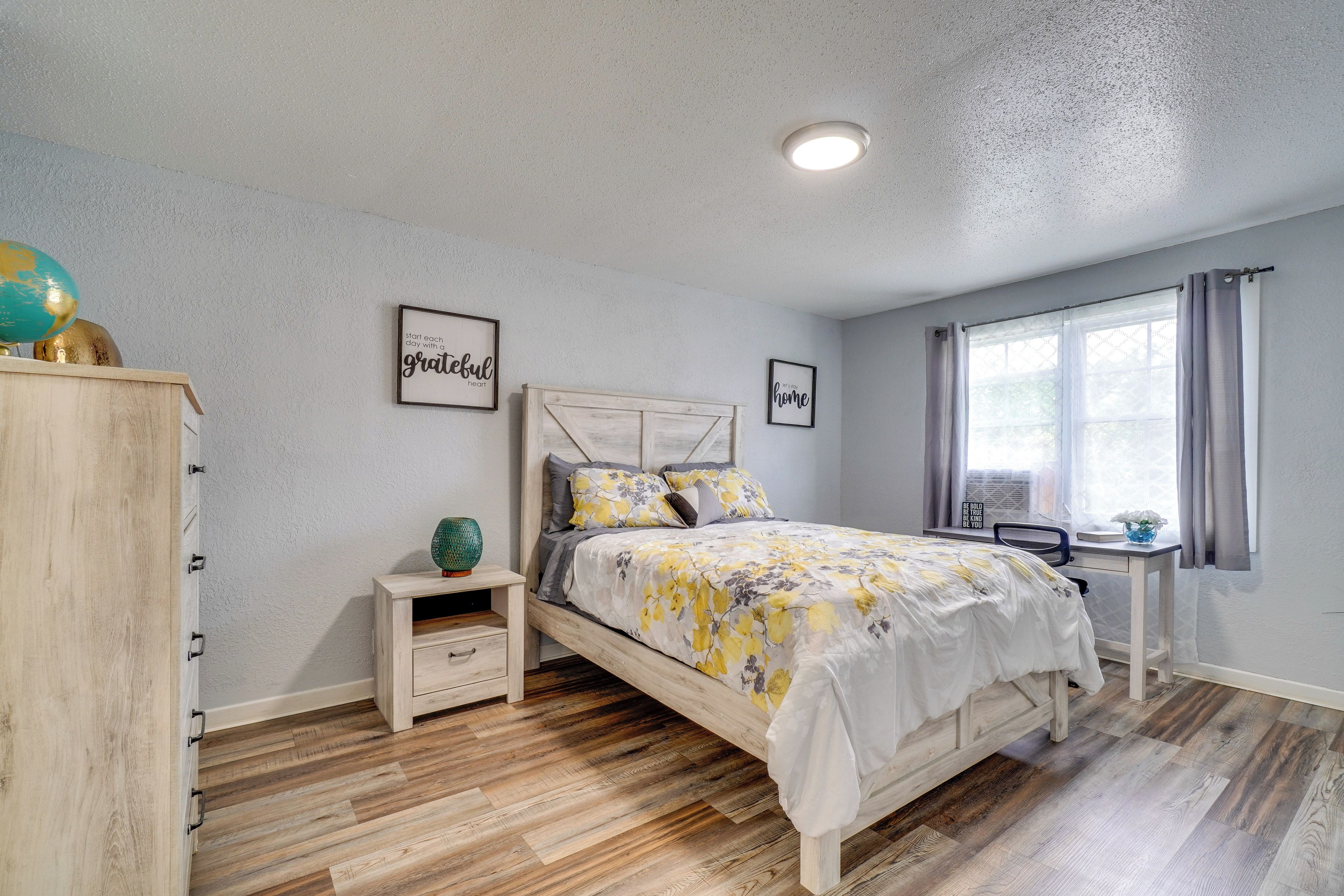 A bedroom with a bed, bedside table, nightstand, and a window with curtains.