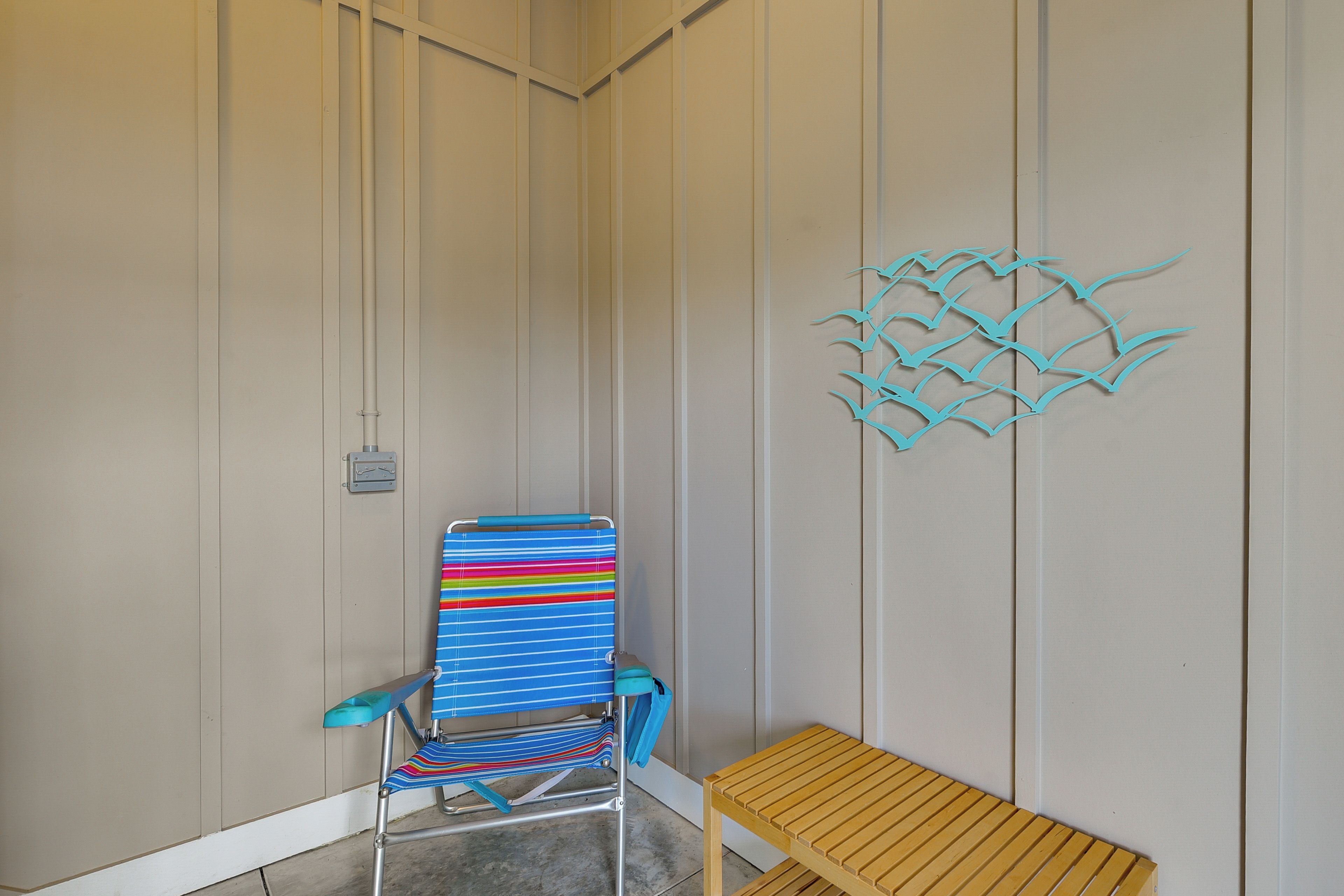 Una habitación con una silla de playa a rayas, un banco de madera y un adorno en la pared.
