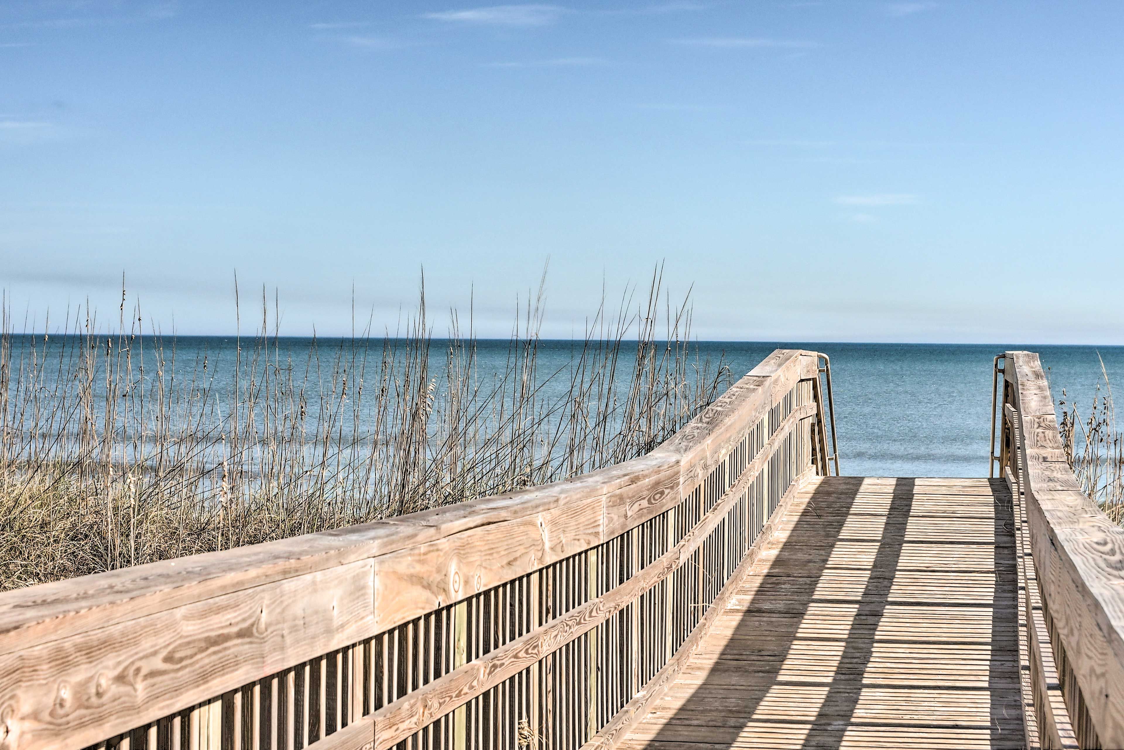 A wooden boardwalk leading to the water with a clear view of the sea.