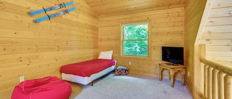 Une pièce de cabane en bois comprenant un lit, un téléviseur, une fenêtre et un pouf rouge.