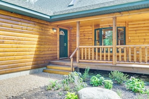 A wooden cabin with a porch, steps leading to a green door, and a garden with plants and rocks.
