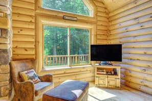 A log cabin interior with a television, a cushioned bench, and a stone wall. - Ski, Hike & Explore! Spacious Conway Cabin w/ Deck (Conway)