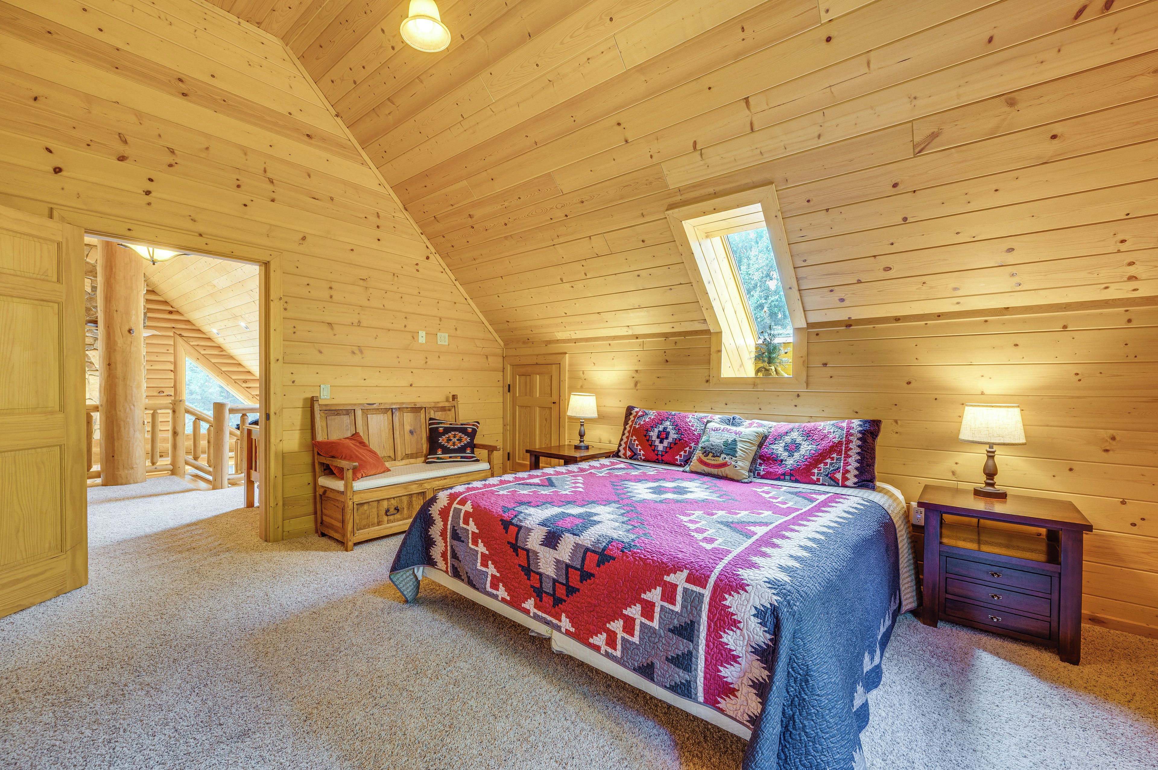Un dormitorio tipo cabaña de troncos con una cama, mesitas de noche, un banco y una ventana.