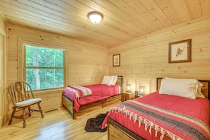 Habitación de cabaña de madera con dos camas, una ventana, una silla y un cuadro en la pared.