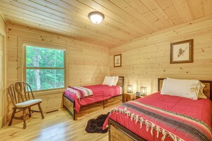 Habitación de cabaña de madera con dos camas, una ventana, una silla y un cuadro en la pared.
