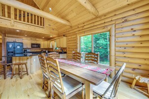 Interior de una cabaña de madera con cocina, comedor y ventanas grandes.