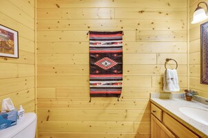 Un baño con paredes de madera, una toalla colgando, un lavamanos y un cuadro enmarcado.