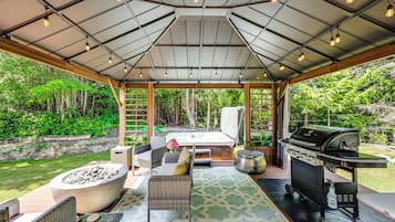 An outdoor covered patio with a hot tub, seating area, and a grill.