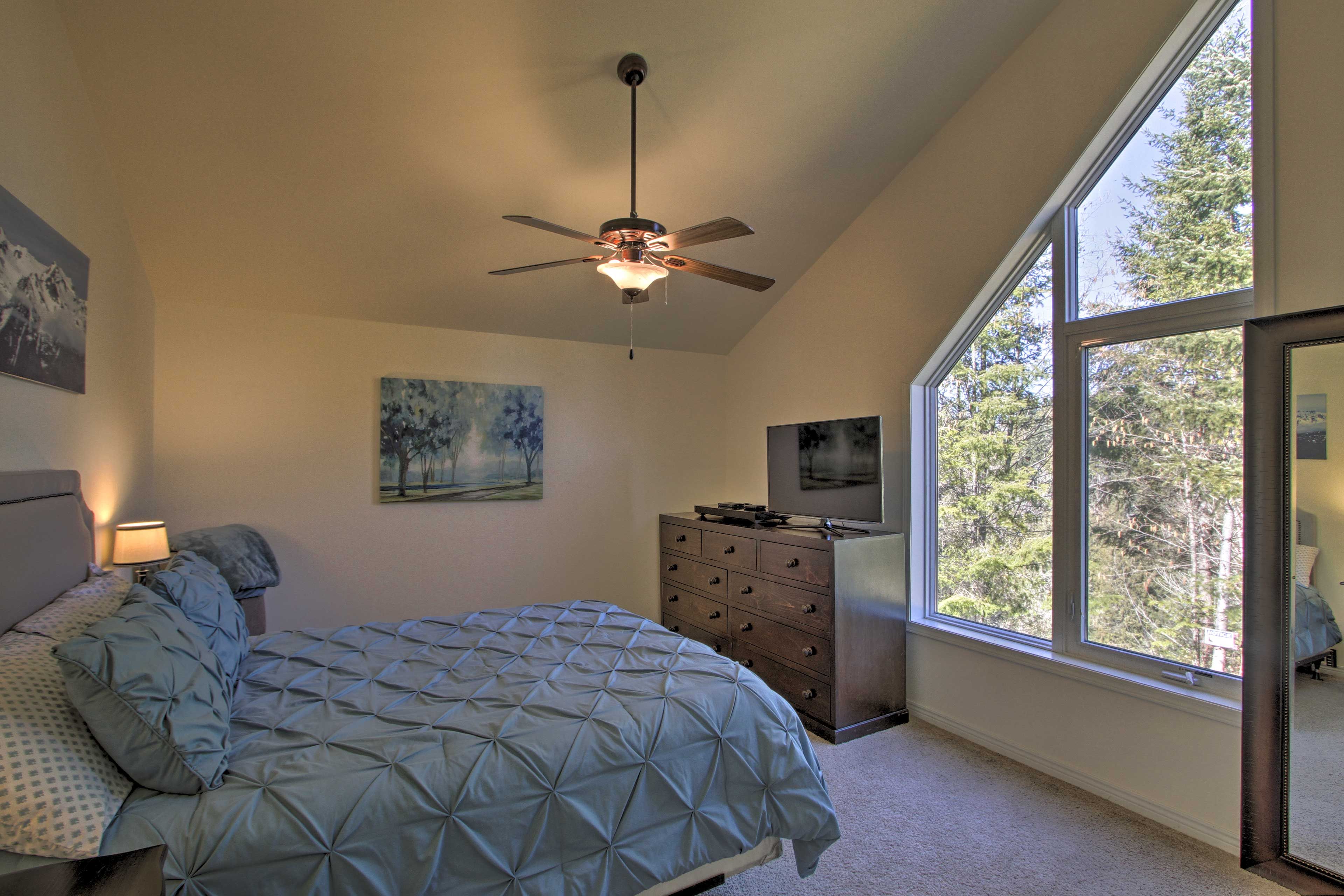 A bedroom with a bed, dresser, ceiling fan, and large windows.