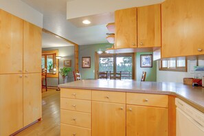 A kitchen with wooden cabinets, a countertop, and a view of the outdoors. - Riverfront Group Getaway Near Glacier NP (Columbia Falls)