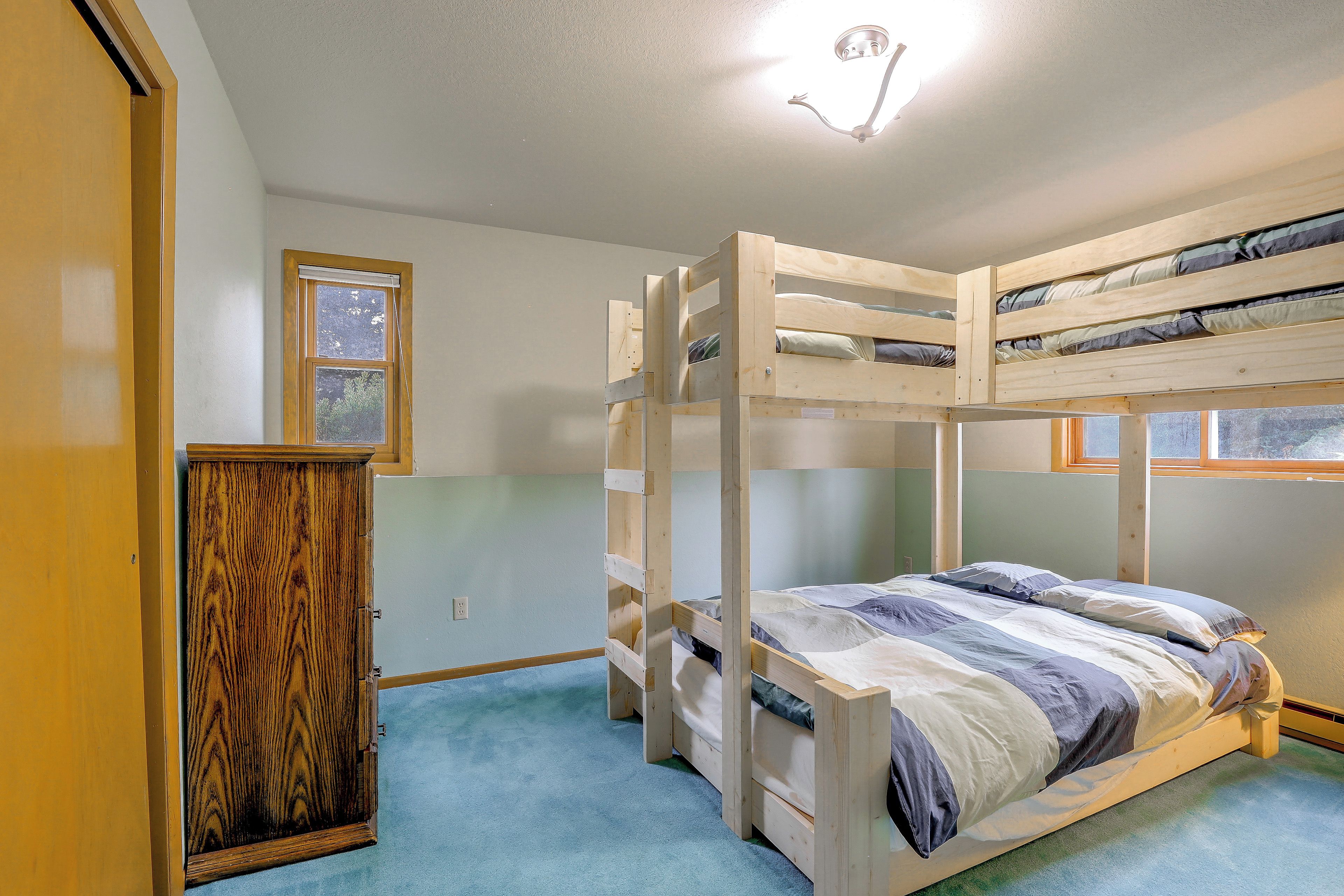 A bunk bed room with a wooden wardrobe and a window.