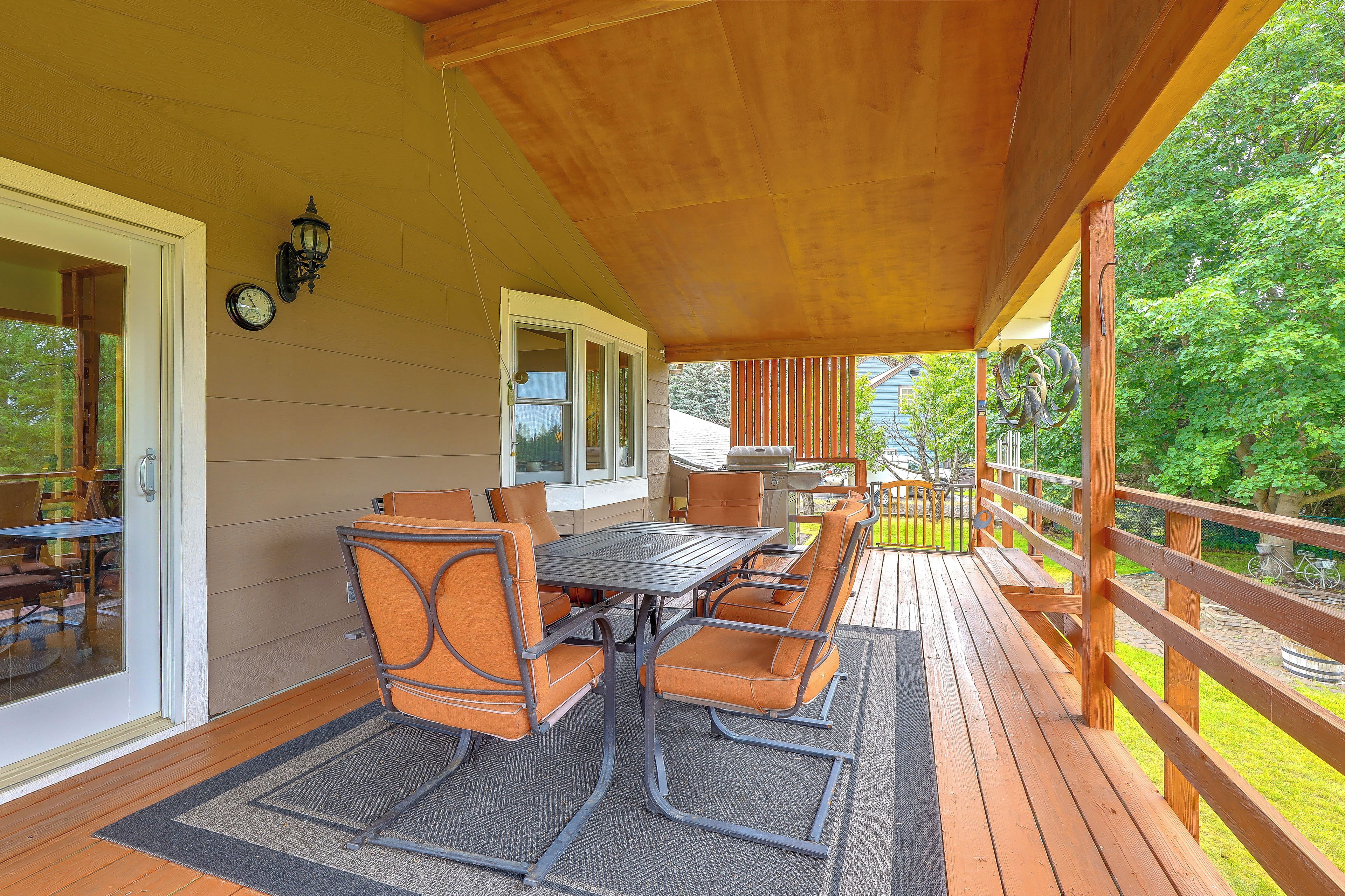 An outdoor patio with a wooden deck, a table with chairs, and a grill.