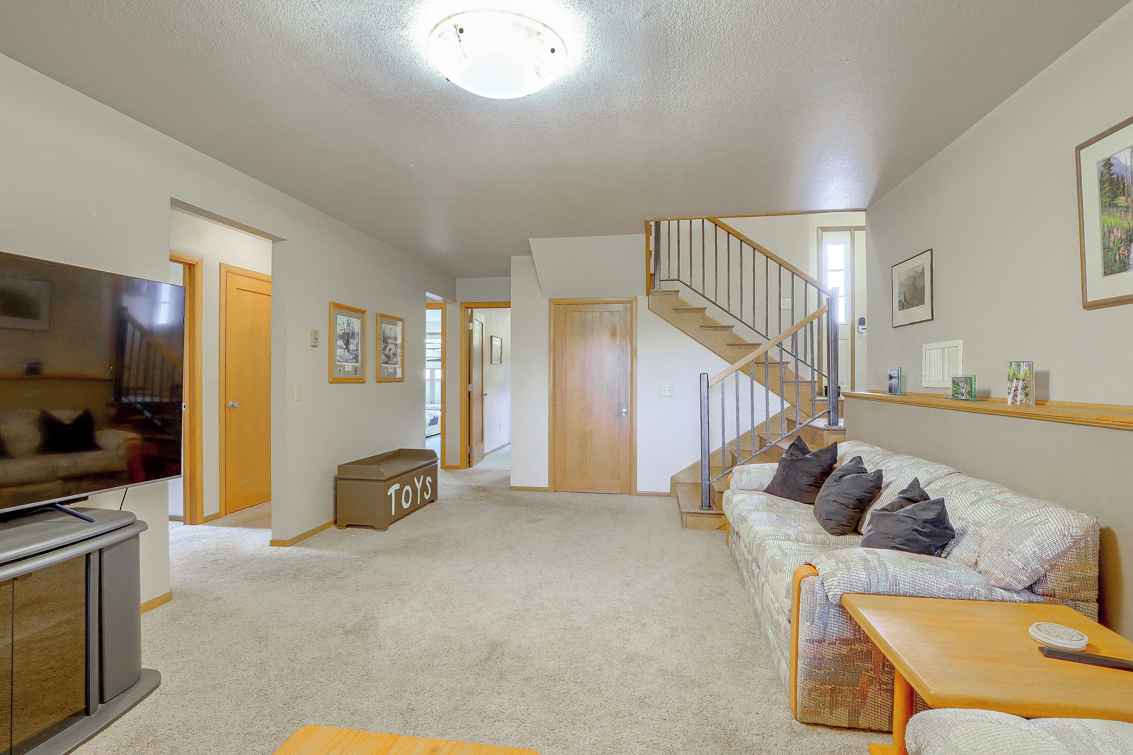A living room with a sofa, a television, a staircase, and a door leading to another room.