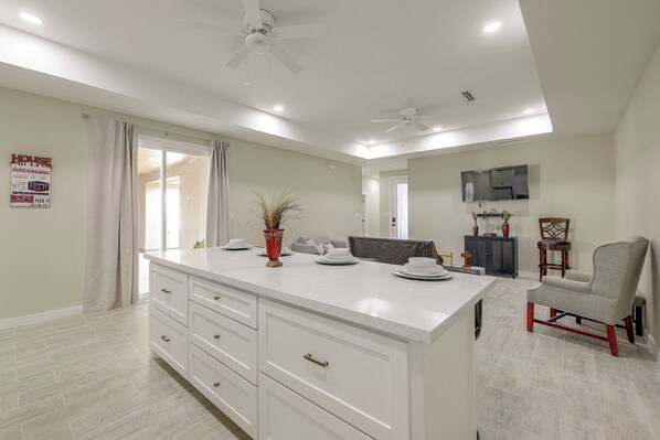 Una cocina moderna con una isla grande, armarios blancos y un ventilador de techo.