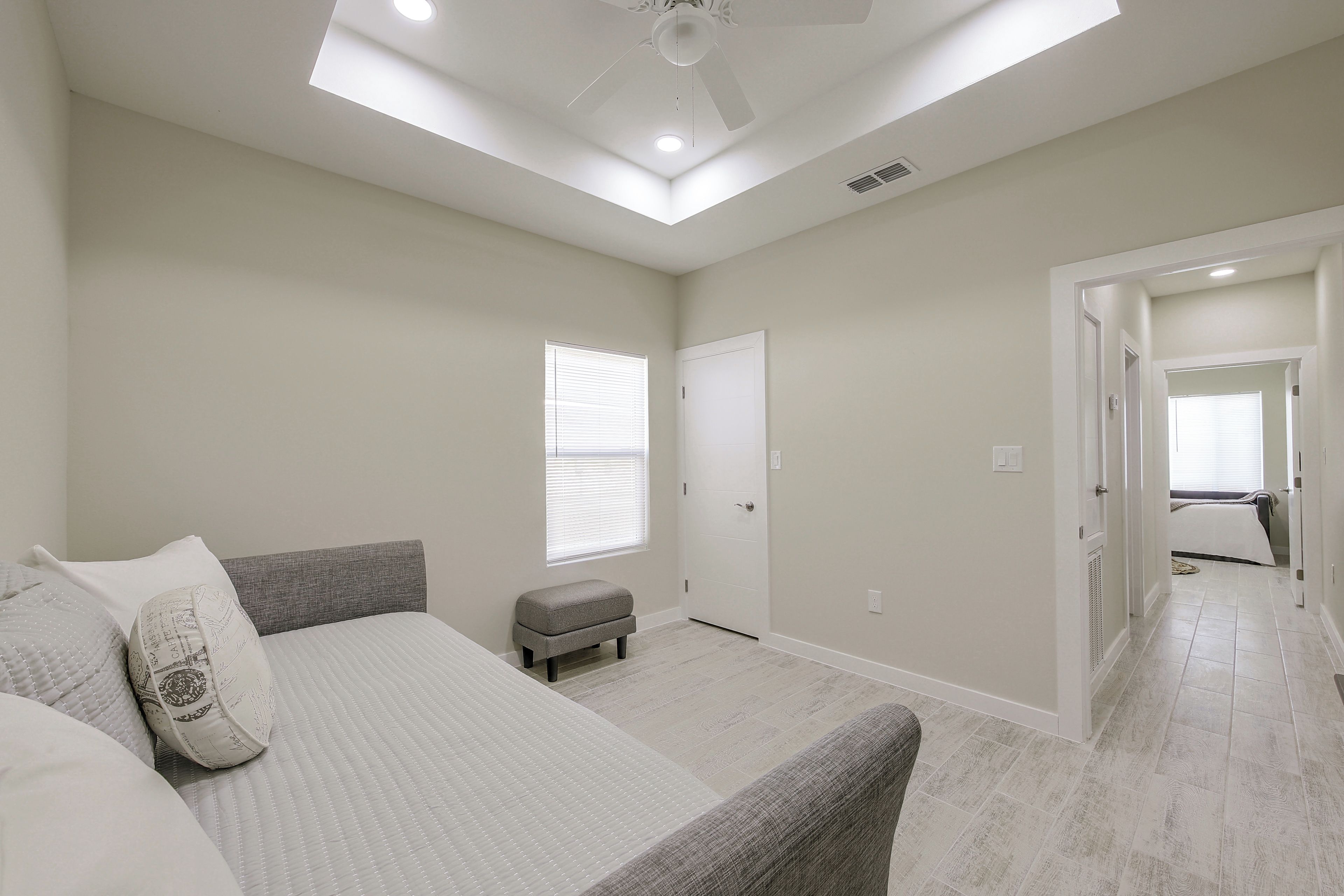 A bedroom with a bed, an ottoman, a ceiling fan, and a skylight.