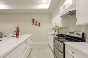 Una cocina moderna con armarios blancos, una estufa de acero inoxidable y una encimera con un jarrón de plantas secas.