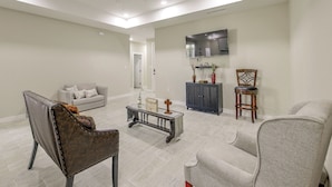 Un salon spacieux avec un canapé gris, un fauteuil en cuir foncé, une table basse et un téléviseur fixé au mur.