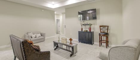 A spacious living room with a grey sofa, a dark leather chair, a coffee table, and a television mounted on the wall.