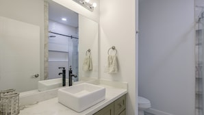 Une salle de bain avec un grand miroir, un lavabo blanc, des toilettes et un espace douche.