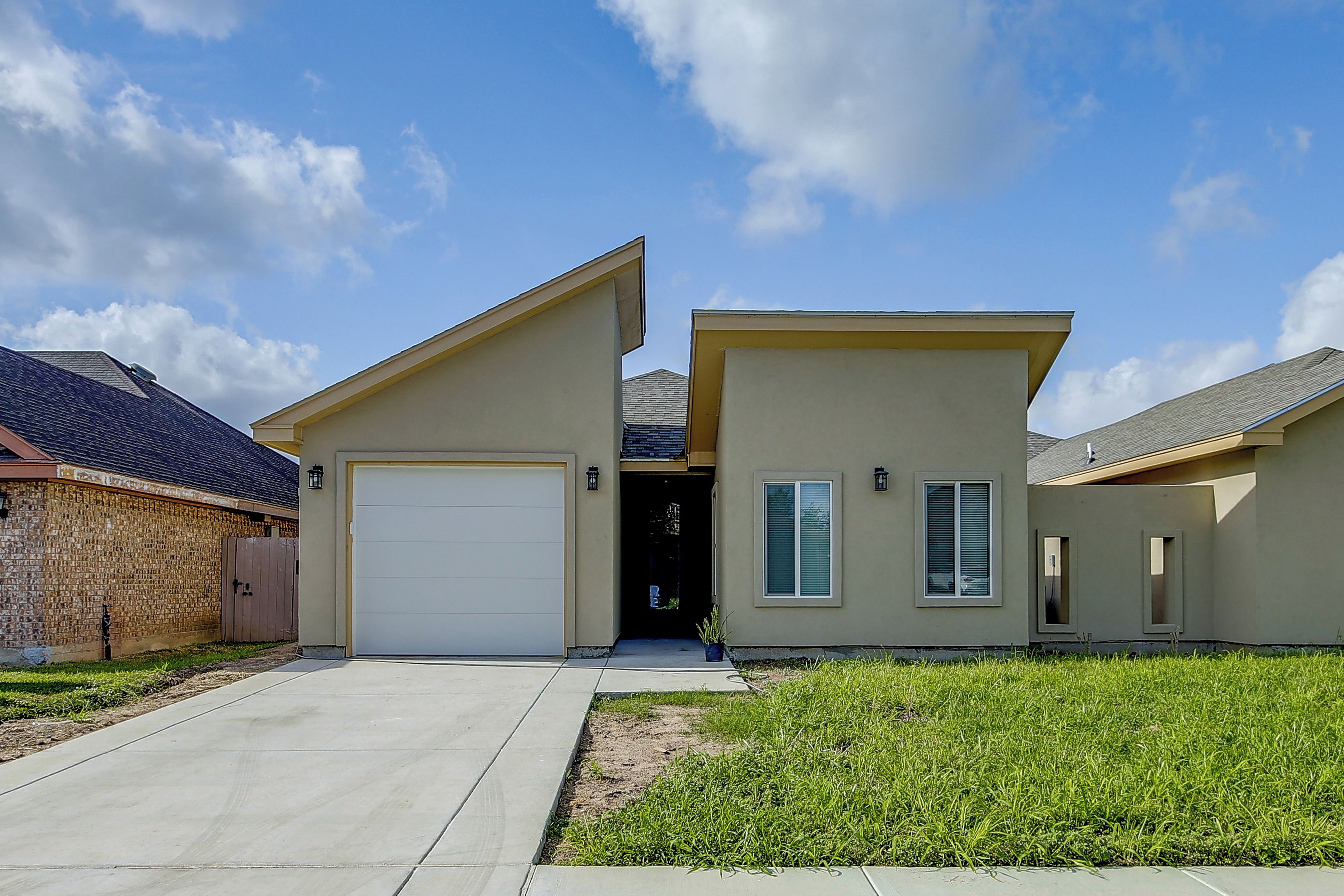 A two-story residential building with a garage, a front door, and a small front yard with grass.