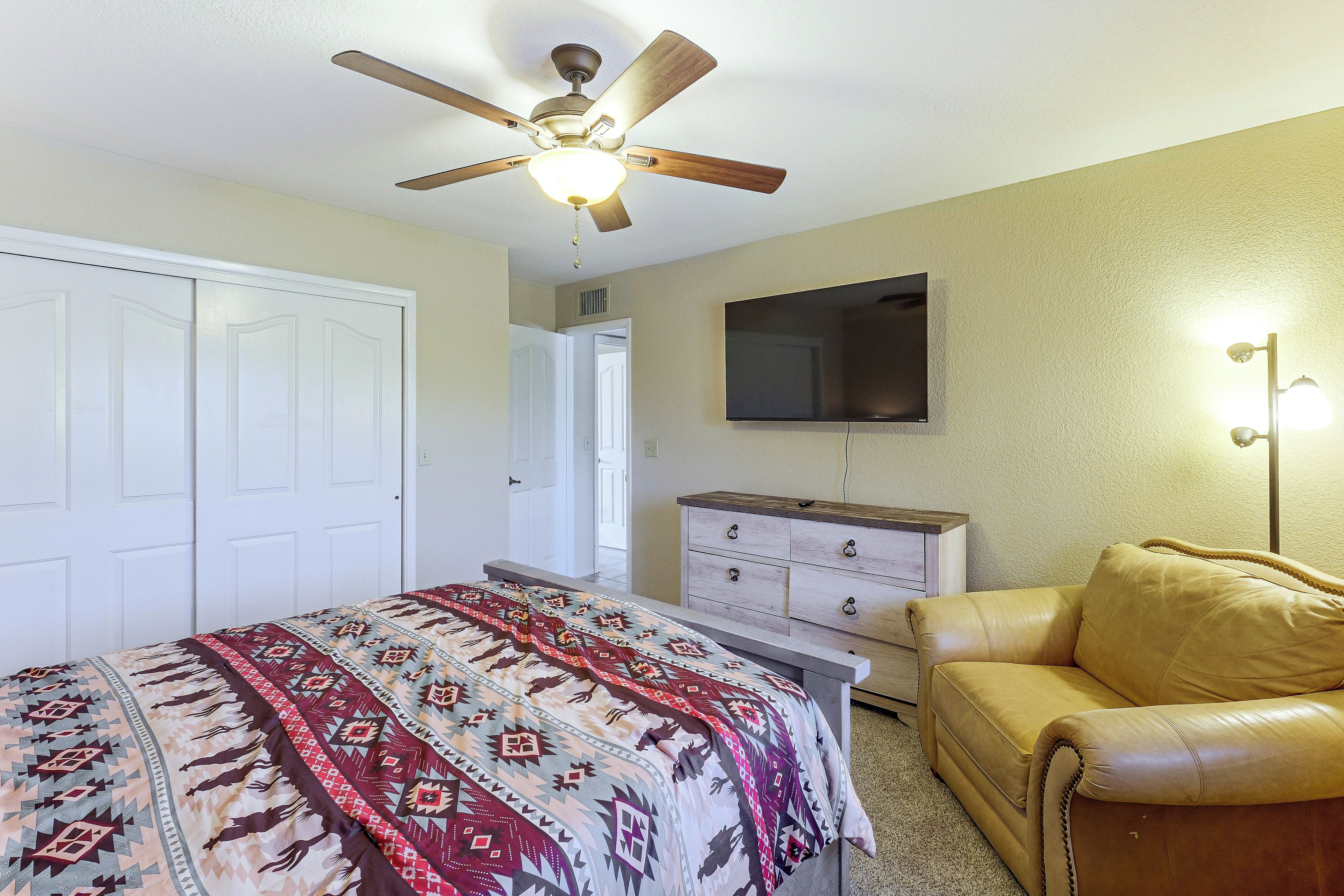 A bedroom with a bed, a dresser, a chair, a ceiling fan, and a television.