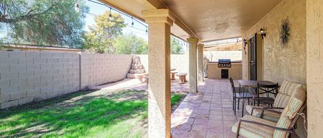 A covered patio area with outdoor seating, a barbecue grill, and a view of the backyard.