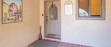 A house entrance with a tiled floor, a door with a glass panel, a welcome sign, and a window with blinds.