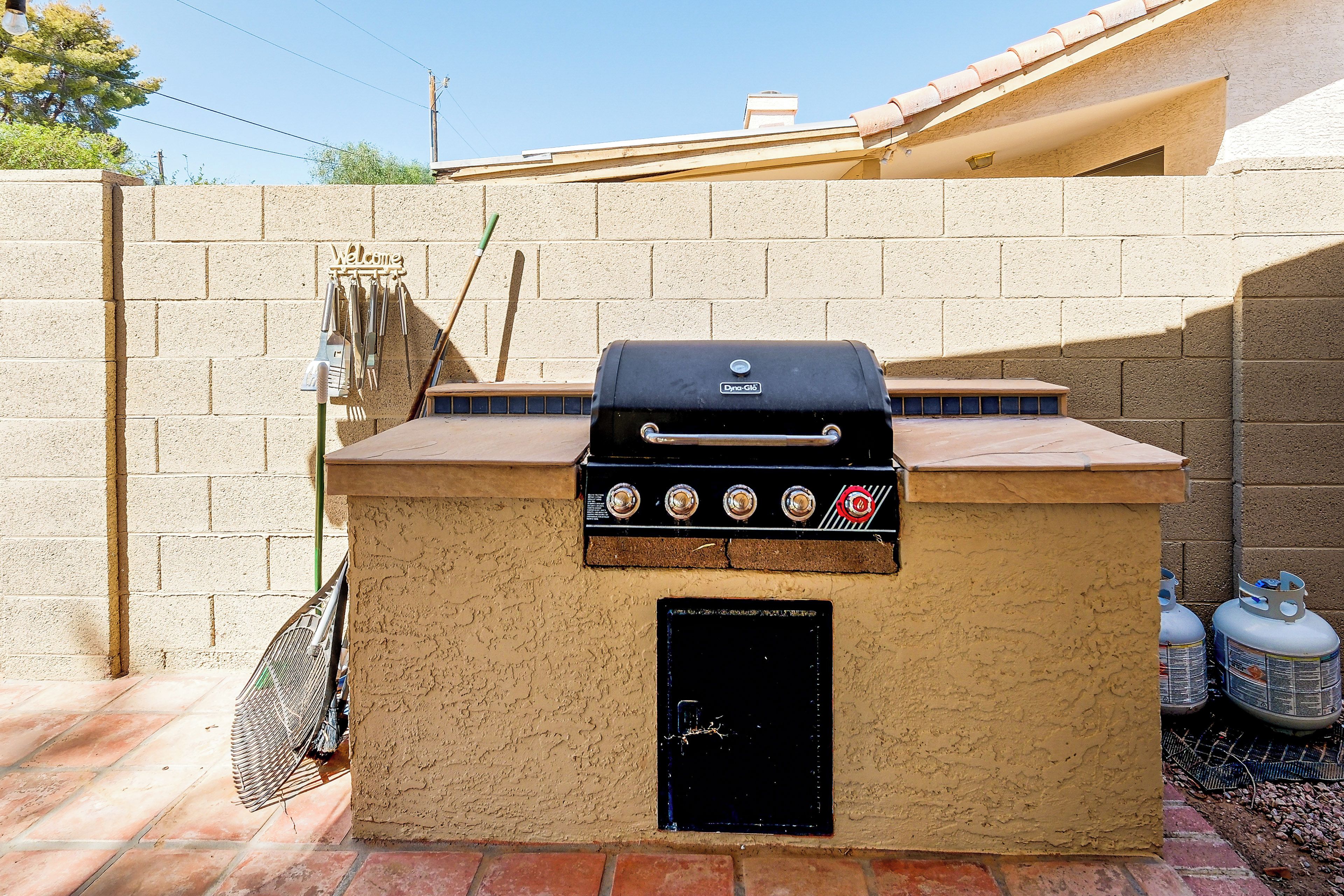 A barbecue grill with a control panel, a welcome sign, and a broom leaning against the wall.