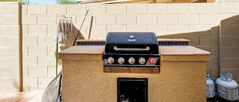 A barbecue grill with a control panel, a welcome sign, and a broom leaning against the wall.