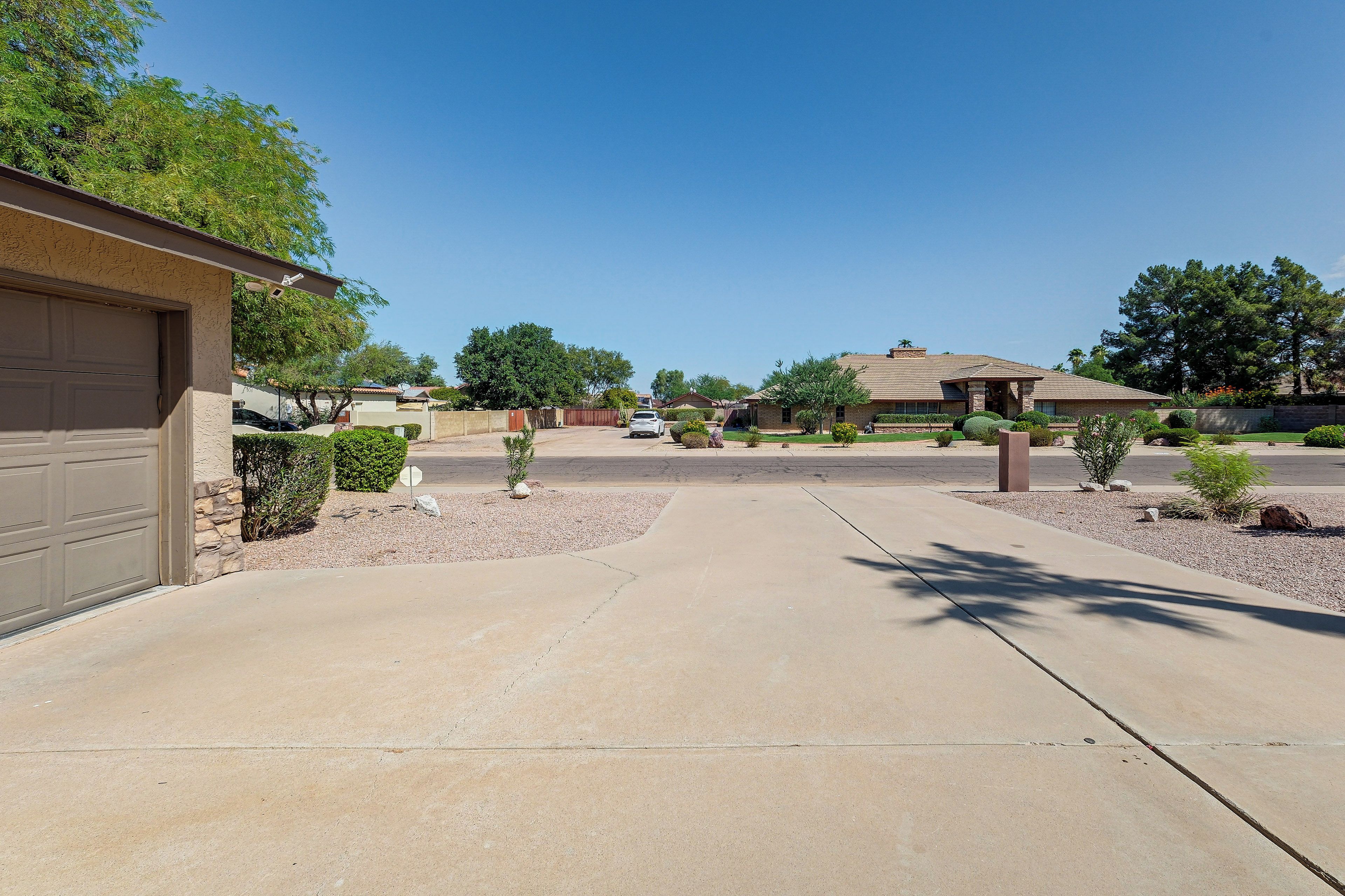 A residential driveway leading to a house with a garage, surrounded by landscaped areas and trees.