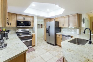 Cozinha moderna com bancadas de granito, eletrodomésticos de aço inoxidável e armários de madeira.