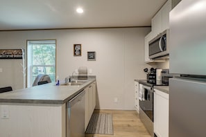 A modern kitchen with a central island, stainless steel appliances, and a view to the outdoors. - Brand New! Peaceful Wooded Retreat in Holcombe! (Holcombe)