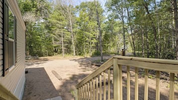 A wooden deck with a staircase leading to a covered area, surrounded by a forested landscape.