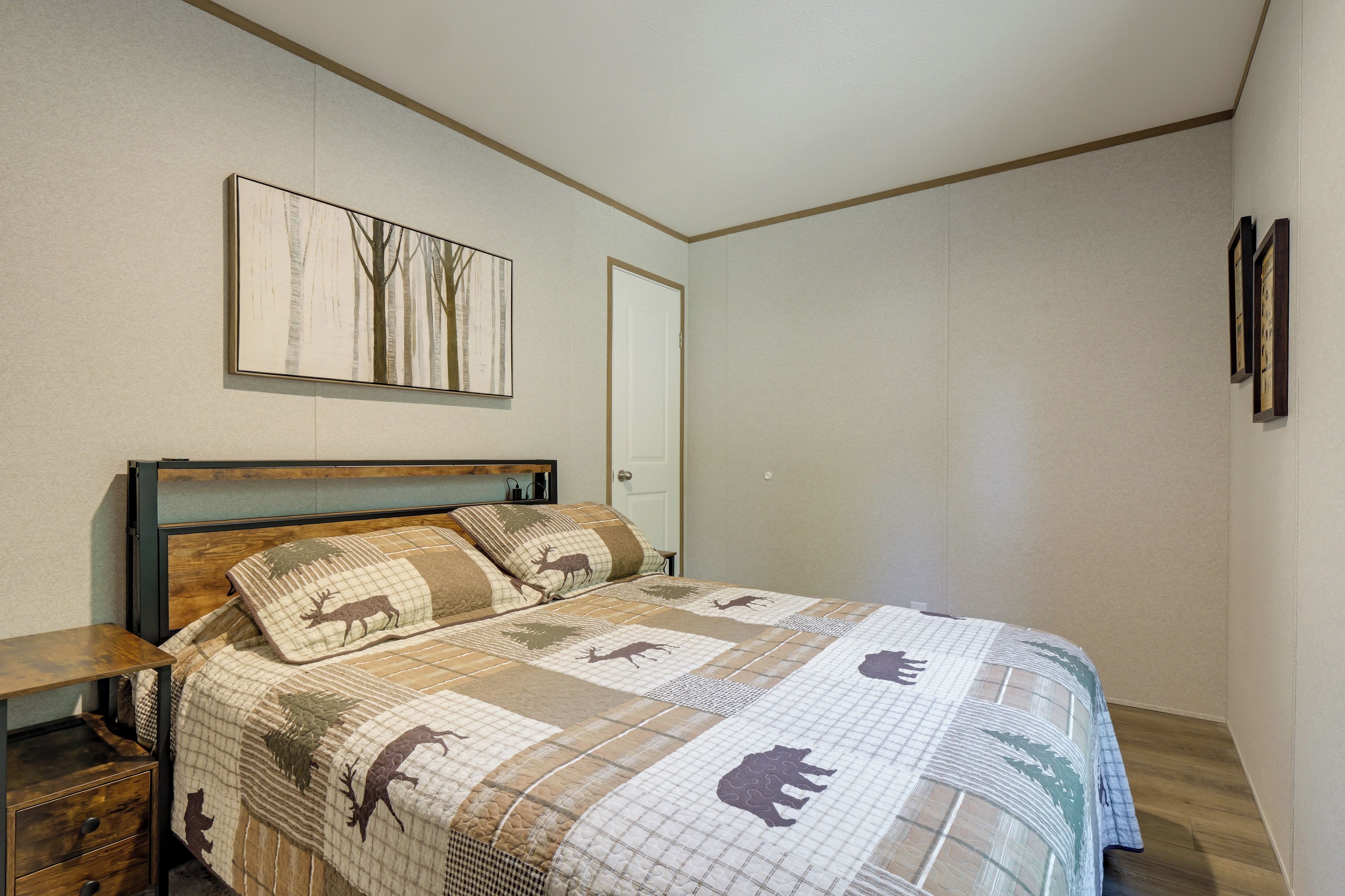 A bedroom with a bed, a nightstand, a door, and a wall-mounted picture.