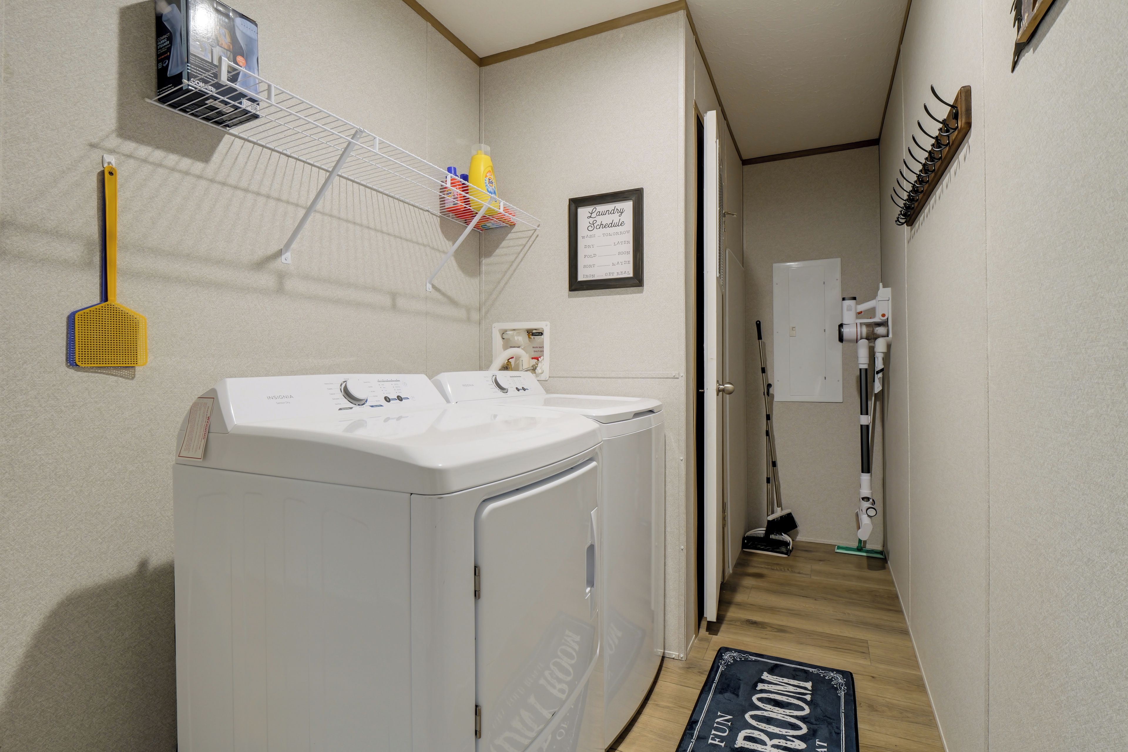 A laundry room with two washing machines, a drying rack, and a laundry schedule sign.
