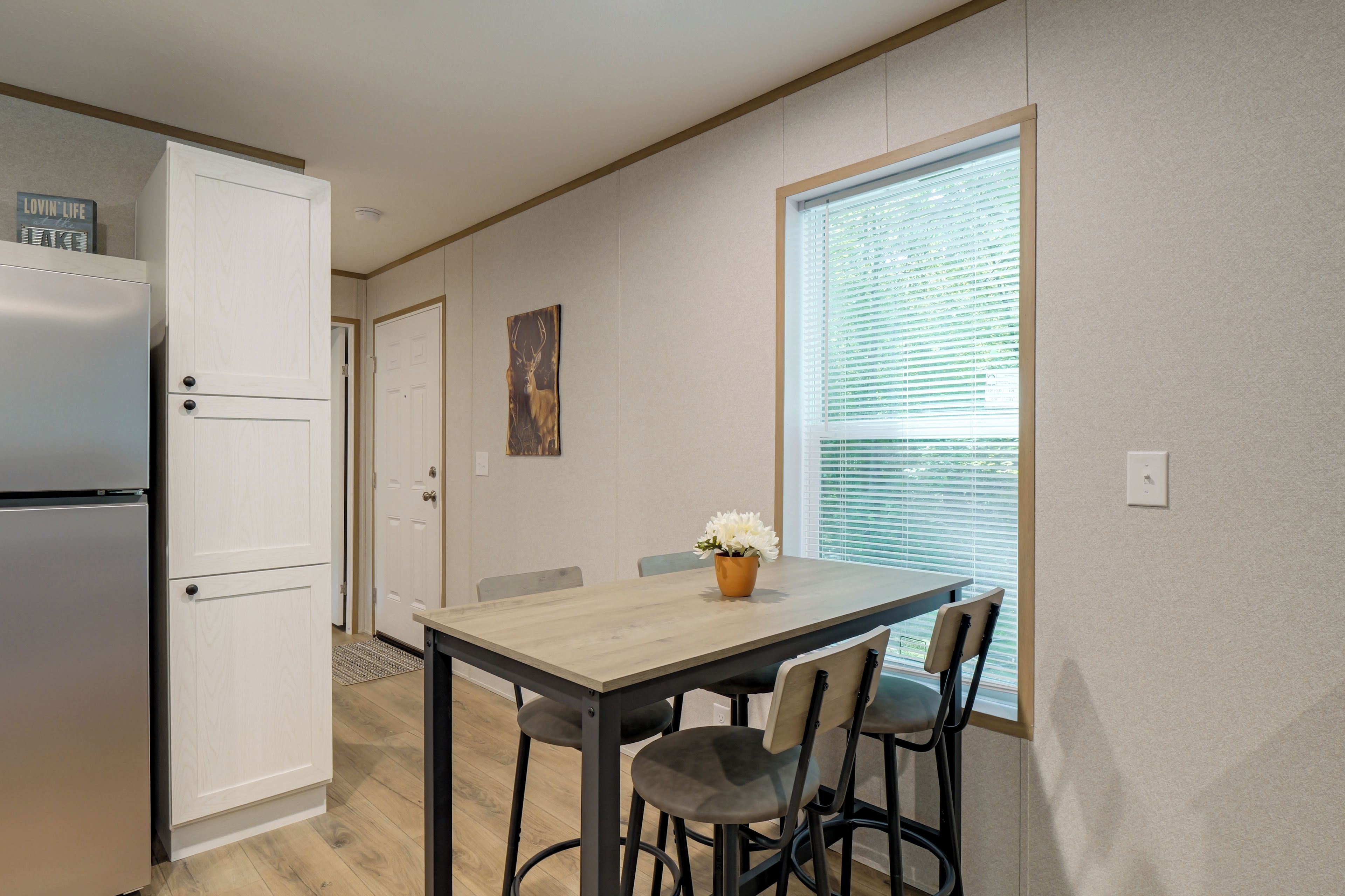 A compact kitchen with a refrigerator, a dining table with chairs, and a window with blinds.