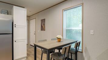 A compact kitchen with a refrigerator, a dining table with chairs, and a window with blinds.