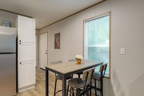 A compact kitchen with a refrigerator, a dining table with chairs, and a window with blinds. - Brand New! Peaceful Wooded Retreat in Holcombe! (Holcombe)