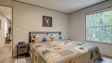 A bedroom with a bed, a nightstand, a digital clock, a window with a forest view, and a wall-mounted deer head artwork.