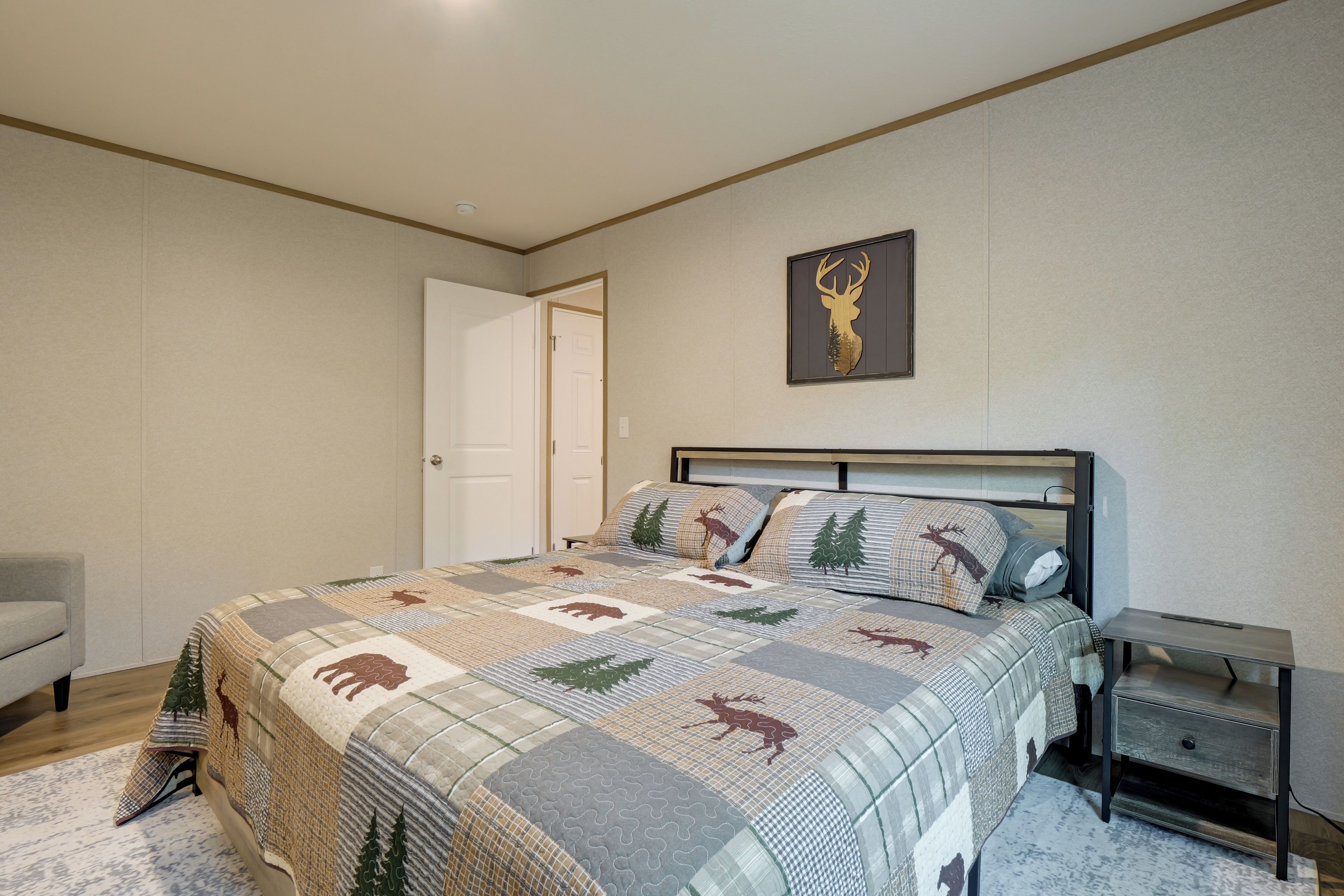 A bedroom with a bed, a nightstand, a door, and a wall-mounted deer head decoration.