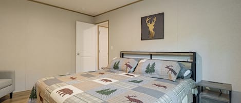 Quarto com cama, mesa de cabeceira, porta e um chifre de veado fixado na parede.