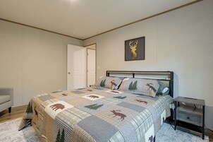 Un dormitorio con cama, mesita de noche, una puerta y un adorno de cabeza de ciervo colgado en la pared.