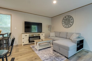 A modern living room with a flat-screen TV, a grey sofa, a coffee table, and a decorative wall clock.