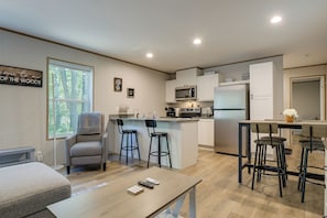 A modern kitchen with a central island, bar stools, a dining table, and a sofa.