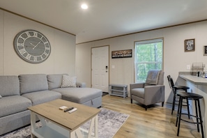 A modern living room with a grey sofa, a wooden coffee table, a grey armchair, and a small bar area with stools.
