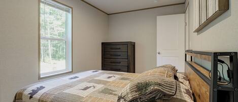 A bedroom with a bed, a dresser, a door, and a window.