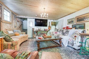 A cozy living room with a wooden ceiling, a chandelier, a television, and a variety of furniture including a sofa, a coffee table, and a chair. - Tryon Equestrian Home Near Wine Country & Hiking (Tryon)