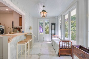 A room with a wooden bench, a bed with a patterned bedspread, and a view of greenery through large windows. - Tryon Equestrian Home Near Wine Country & Hiking (Tryon)