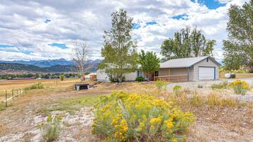 A rural house with a garage, surrounded by dry grassland and yellow flowers, with mountains in the background.