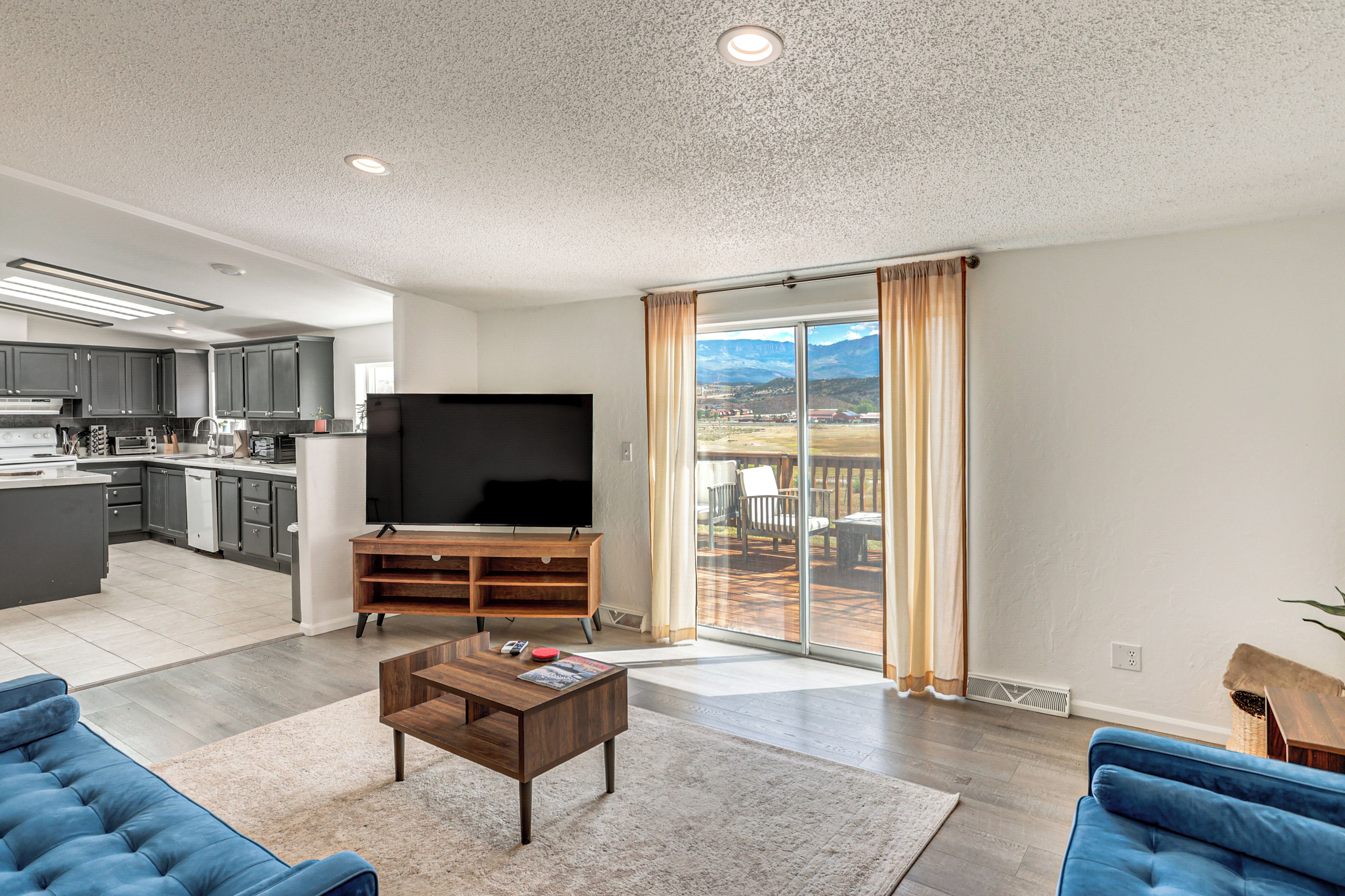 A modern living space with a kitchen, a flat-screen TV, a wooden entertainment unit, and a large sliding glass door leading to a deck.